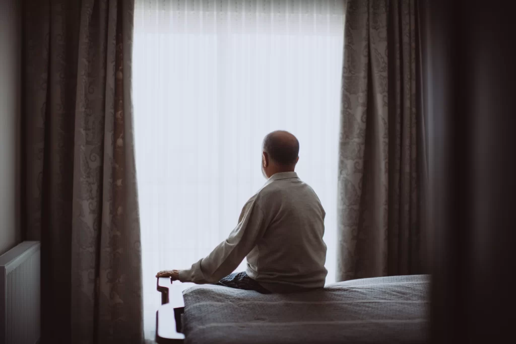 Person sitting on a bed in a dimly lit room, hands on their face, symbolizing emotional struggle after sobriety